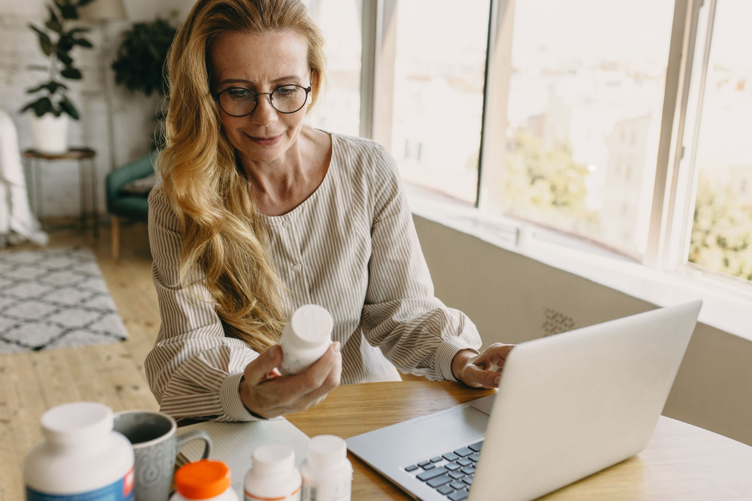 Woman reading supplement bottle at desk with laptop