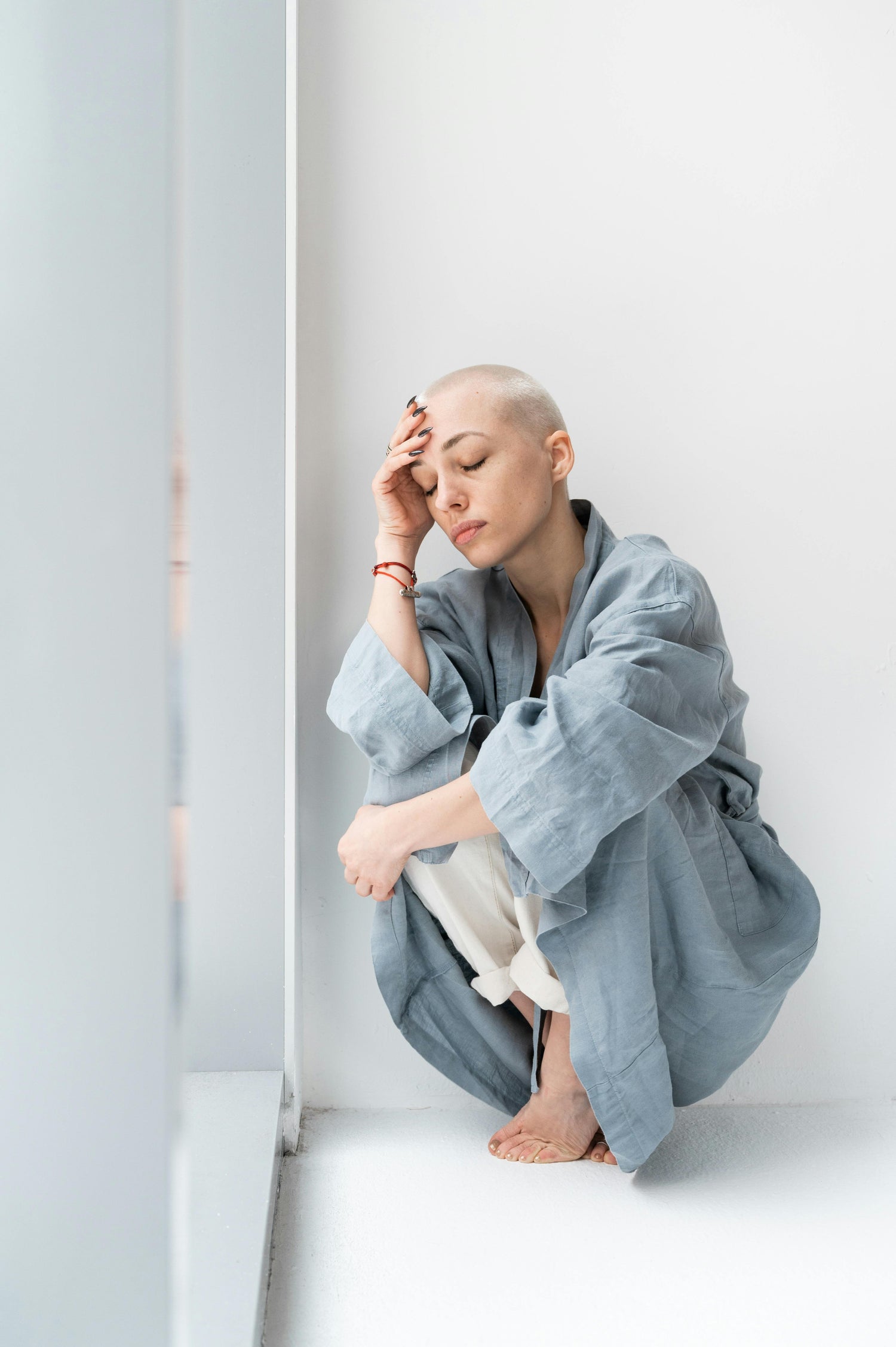 bald woman in meditation pose wearing gray robe indoors