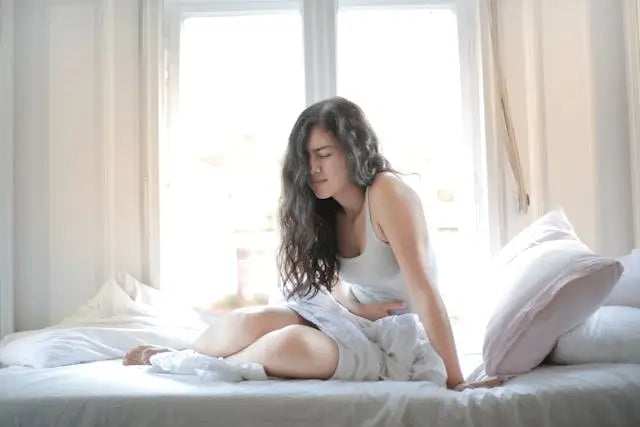 woman experiencing stomach pain sitting on bed
